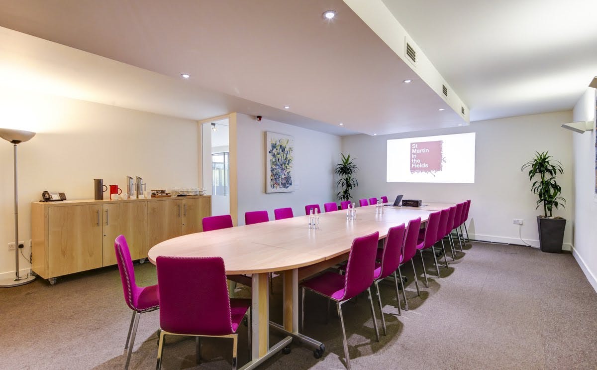 Modern meeting room in St Martin-in-the-Fields with oval table and pink chairs.