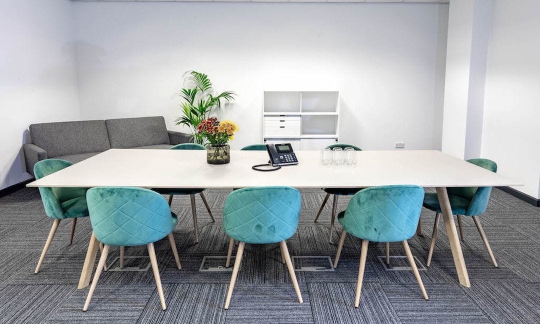 Modern meeting room with white table and teal chairs at Troubadour Brent Cross Studios.