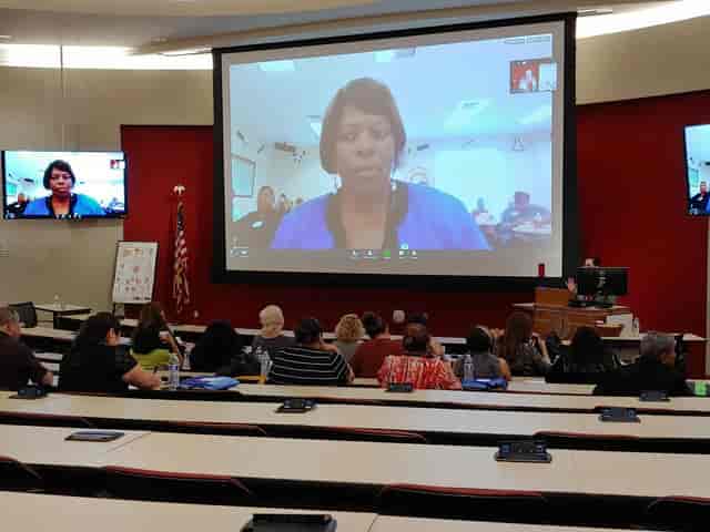 Hybrid meeting setup in Aresty Auditorium with large screen and engaged audience.