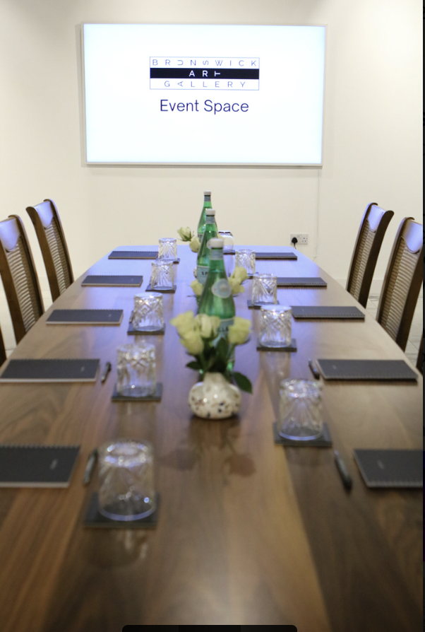 "Elegant meeting setup with wooden table and fresh flowers at Brunswick Art Gallery." - Banner