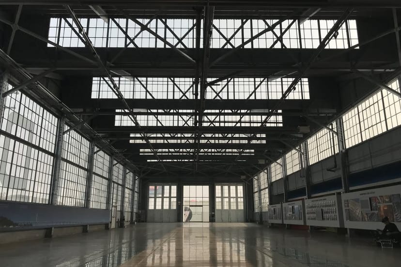 Spacious industrial indoor event space with large windows for exhibitions and corporate gatherings.
