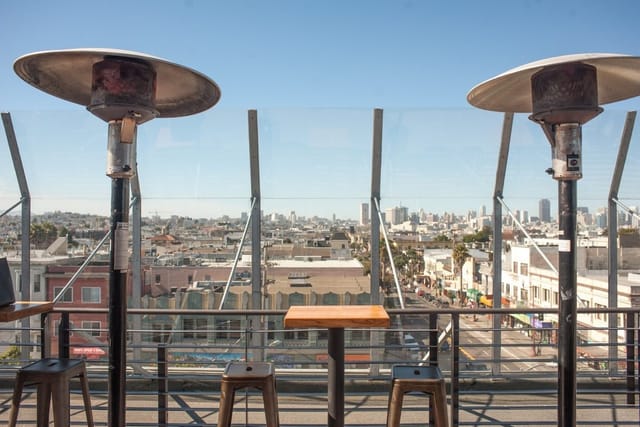 Stylish rooftop patio with heaters and city skyline view, perfect for events and gatherings.