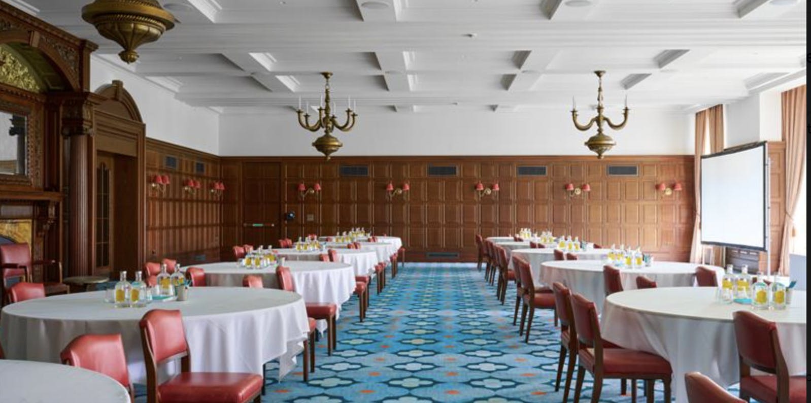 Elegant Ballroom at University Arms Cambridge with round tables and red chairs for events.