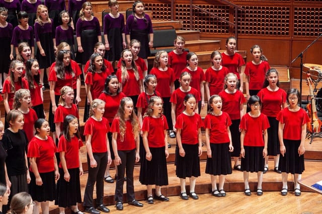 Children's choir in red and black outfits performing on stage at San Francisco event.