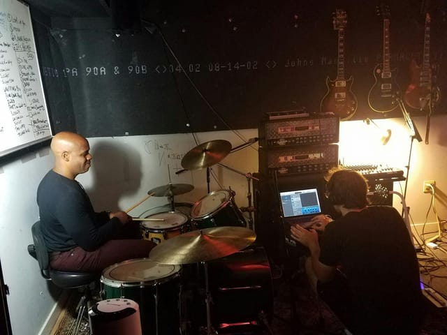 Dynamic rehearsal room with drummer and sound engineer for live event production.