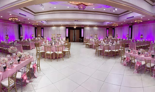 Elegant wedding banquet hall with pink decor, floral centerpieces, and gold chairs.