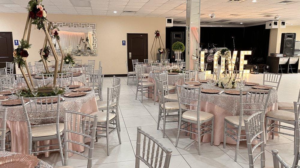 Elegant wedding venue with pink tables, silver chairs, and romantic floral centerpieces.