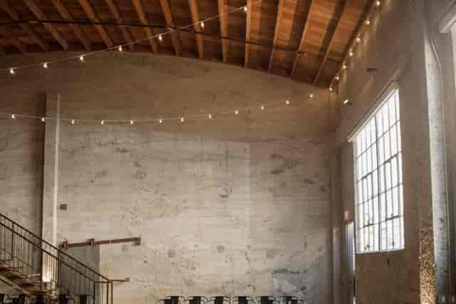 Spacious industrial venue with string lights, ideal for corporate events and celebrations.