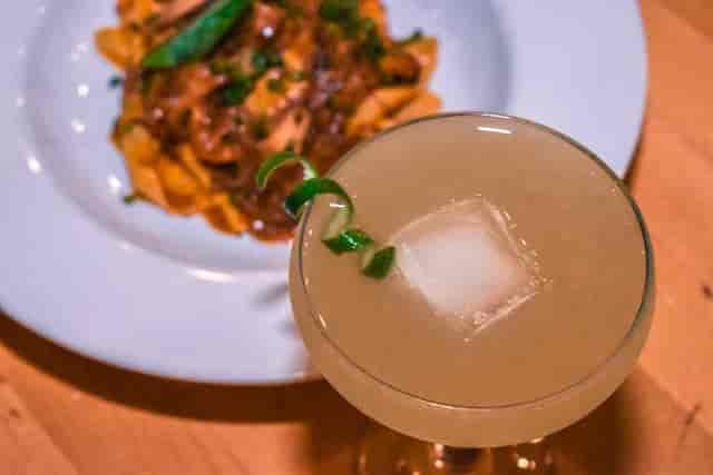 Craft cocktail with ice cube and pasta backdrop for upscale networking events.