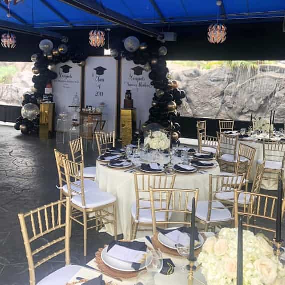 Elegant banquet hall setup for graduation celebration with gold accents and floral centerpieces.