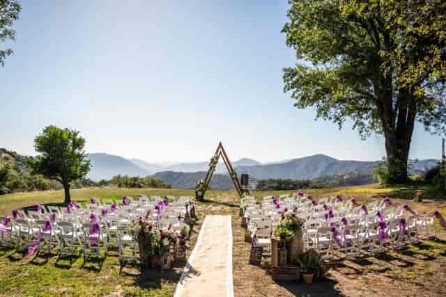 Outdoor wedding setup at Barn in San Diego with purple ribbon chairs and mountain backdrop.