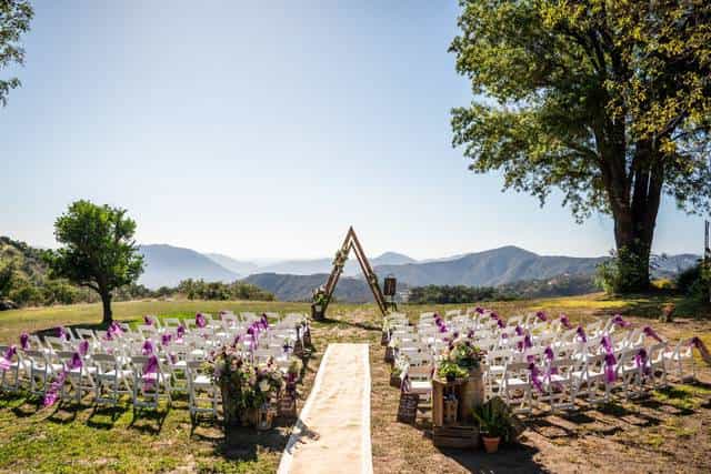 Outdoor wedding setup at Barn in San Diego with purple ribbon chairs and mountain backdrop.