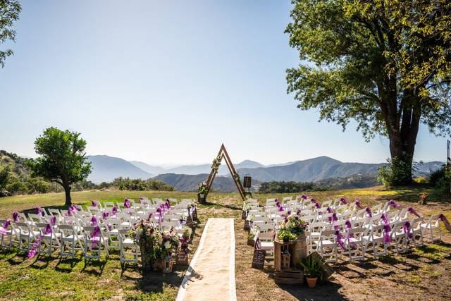 Outdoor wedding setup at Barn in San Diego with purple ribbon chairs and mountain backdrop.