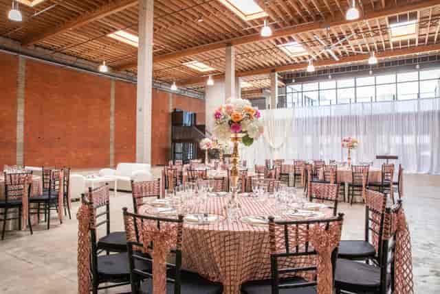Elegant event space with round tables, pink and gold decor for weddings or corporate events.