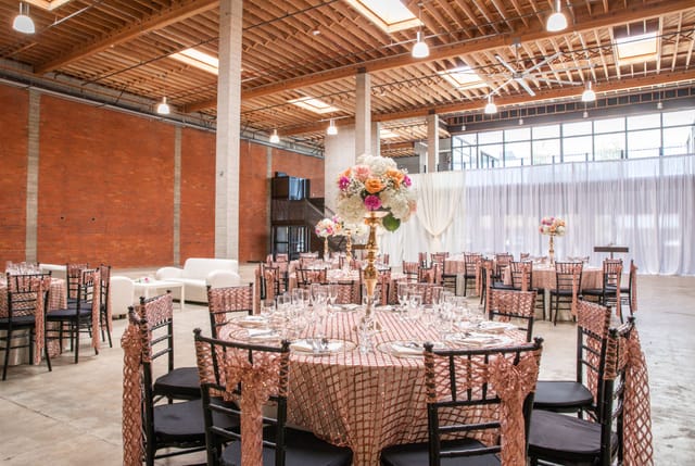 Elegant event space with round tables, pink and gold decor for weddings or corporate events.