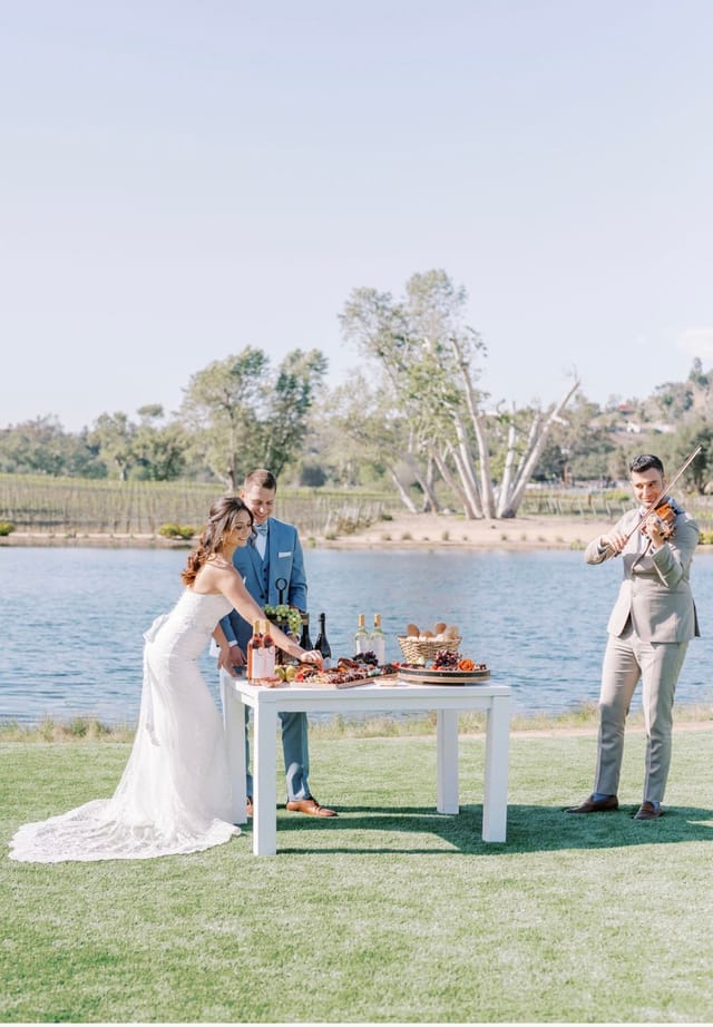 Elegant outdoor wedding setup by a lake with gourmet food and live music.