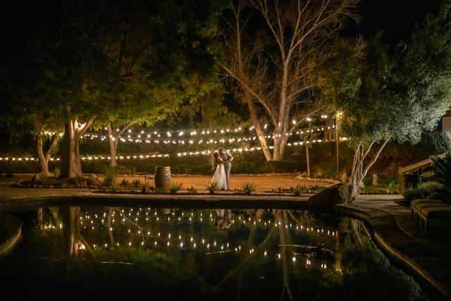 Enchanting outdoor wedding venue with warm string lights and elegant water reflection.