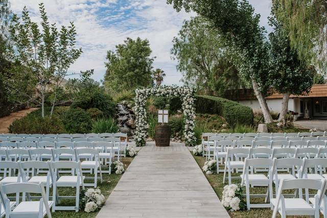 Outdoor wedding ceremony with floral archway and white chairs at Harmony Estate.