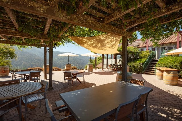 Outdoor patio with rustic tables under pergola, ideal for meetings and events.