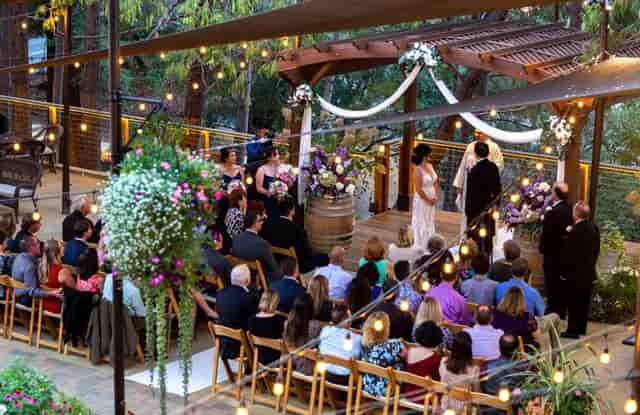 Outdoor wedding ceremony at Testarossa Winery with floral arbor and string lights.