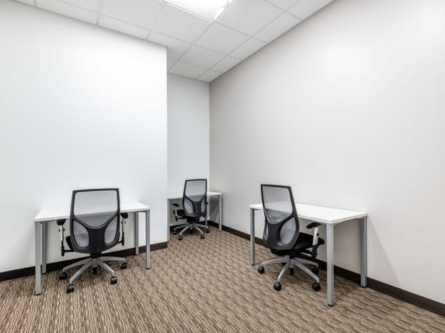 Minimalist coworking meeting space with three workstations for focused discussions.