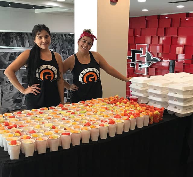 Vibrant taco catering setup with staff, colorful fruit cups for events and healthy options.