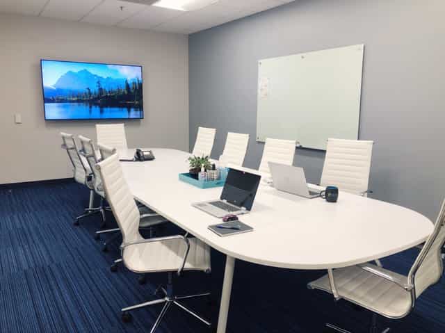 Modern conference room with oval table, laptops, and large screen for effective meetings.