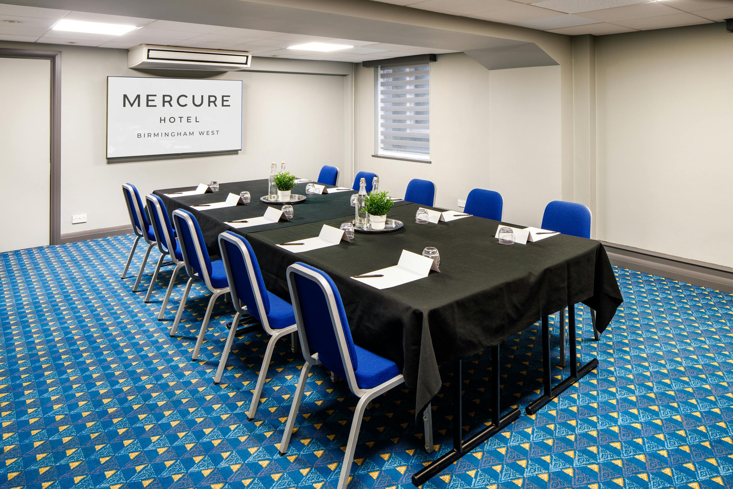 Meeting room at Mercure Birmingham West Hotel with a long table and blue chairs.