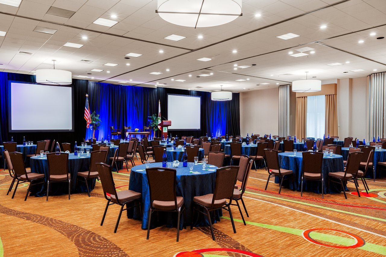 Event space at Holiday Inn Express San Jose, featuring round tables and dual screens for conferences.