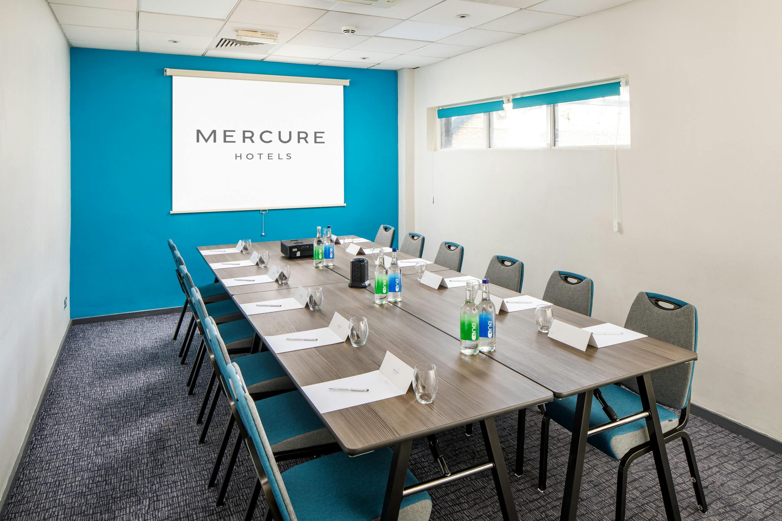 Meeting room at Mercure Bedford with long table, water bottles, and projector screen.