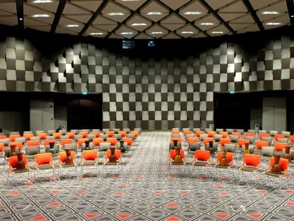 Modern event space with geometric wall, vibrant orange chairs for workshops and meetings.