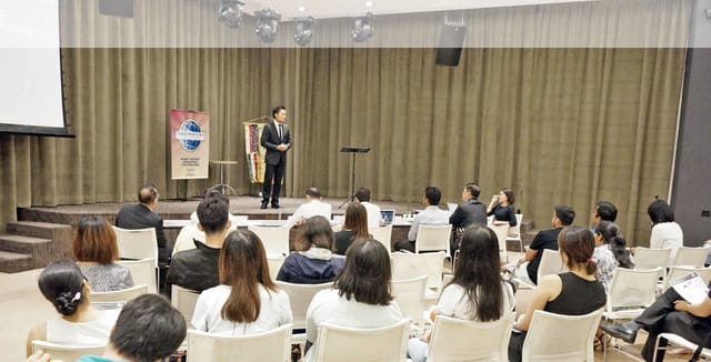 Speaker engaging audience in well-lit LISHA Tamil Toastmasters Club conference room.