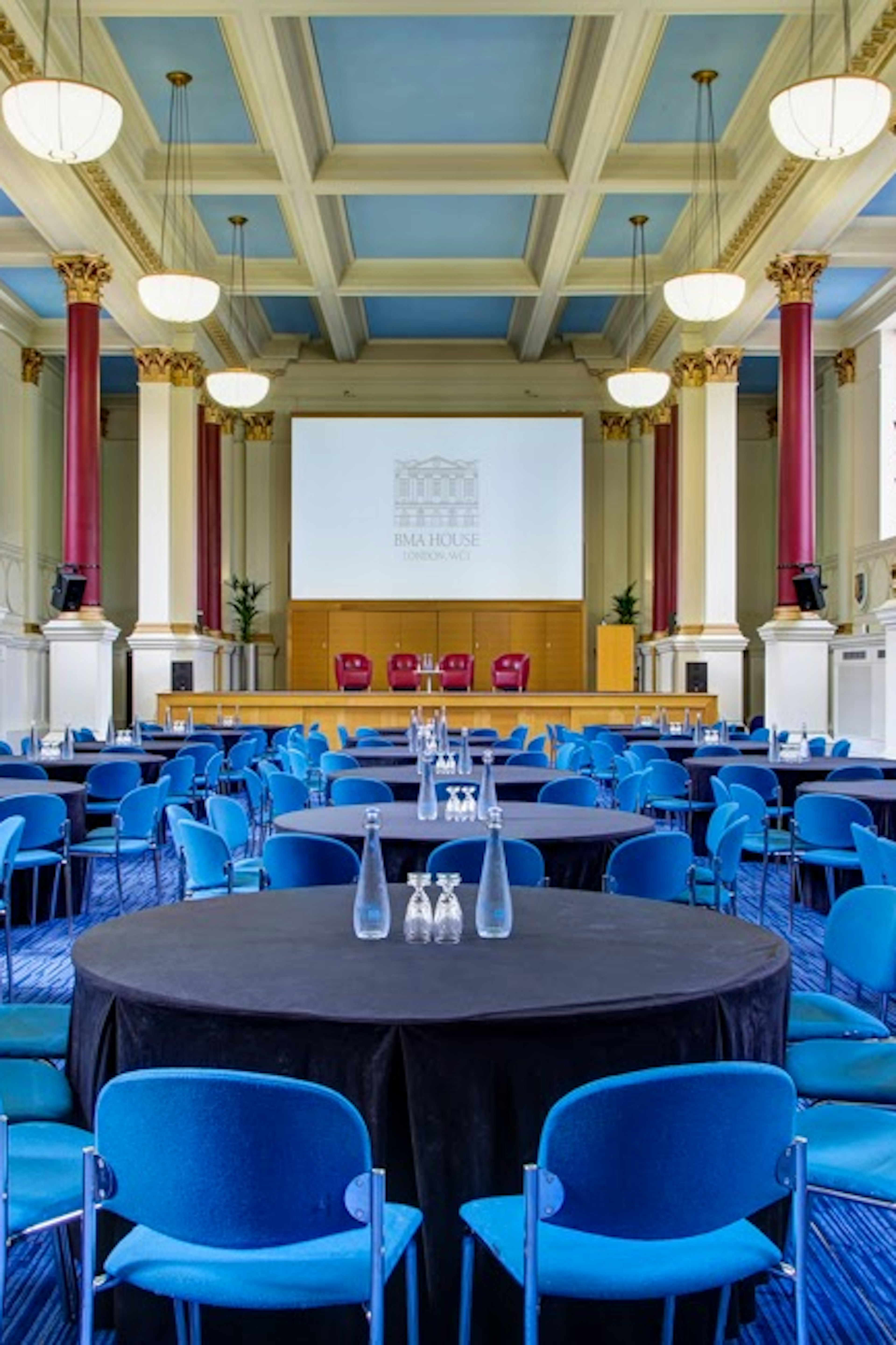 Event space at Tarling East Community Centre with round tables and blue chairs for conferences. - Banner