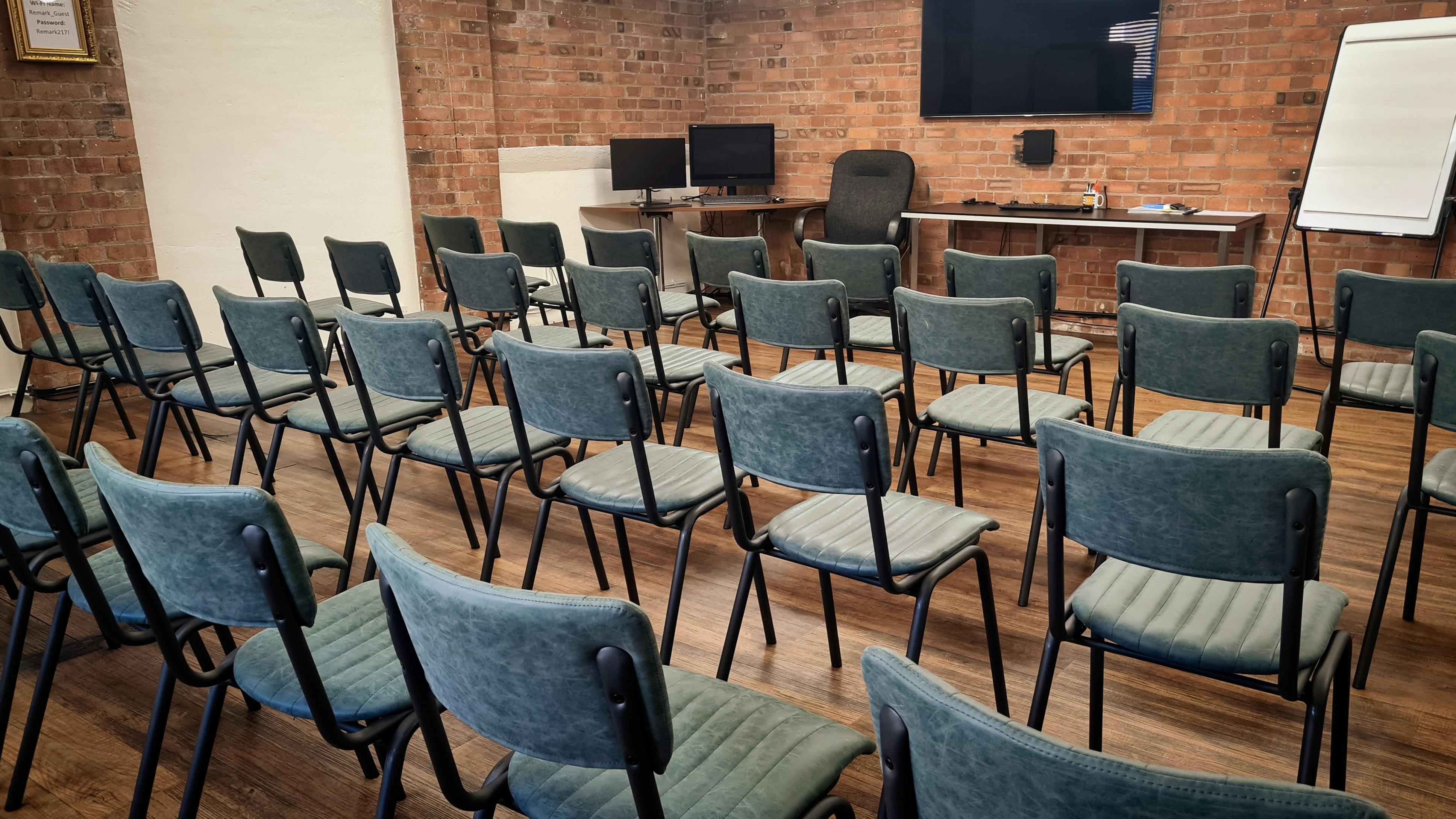 Yellow Room at Remark! Events with chairs, monitors, and a brick wall for meetings.