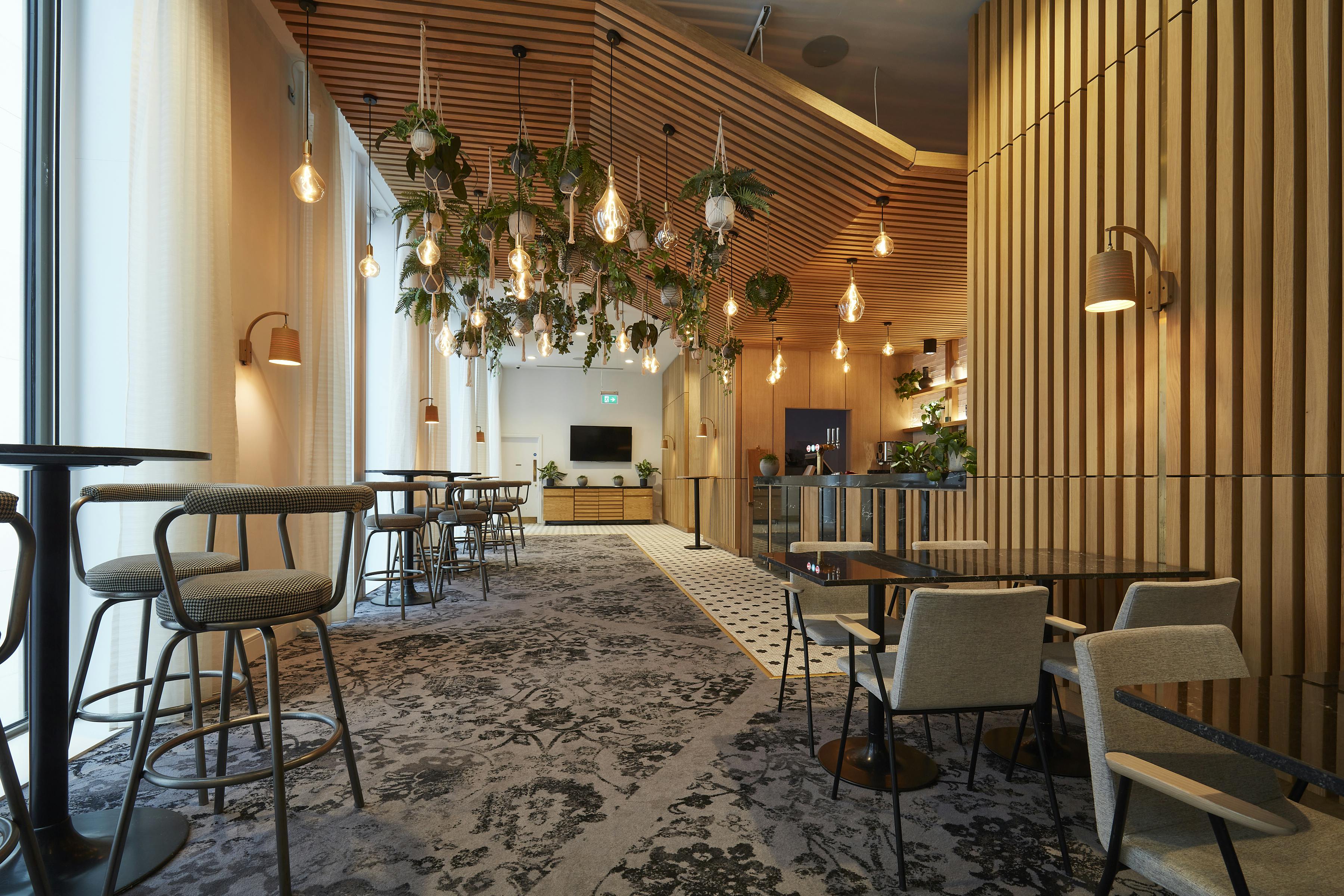 Modern event space at Salvation Bar, voco Manchester, with warm wood accents and plants.