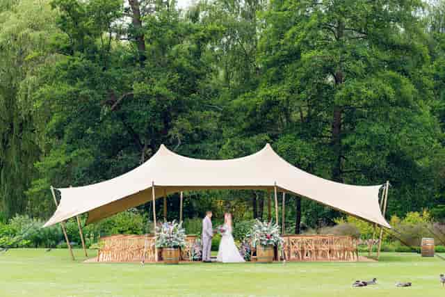 Outdoor wedding ceremony in a marquee at Leeds Castle with rustic chairs and floral decor.
