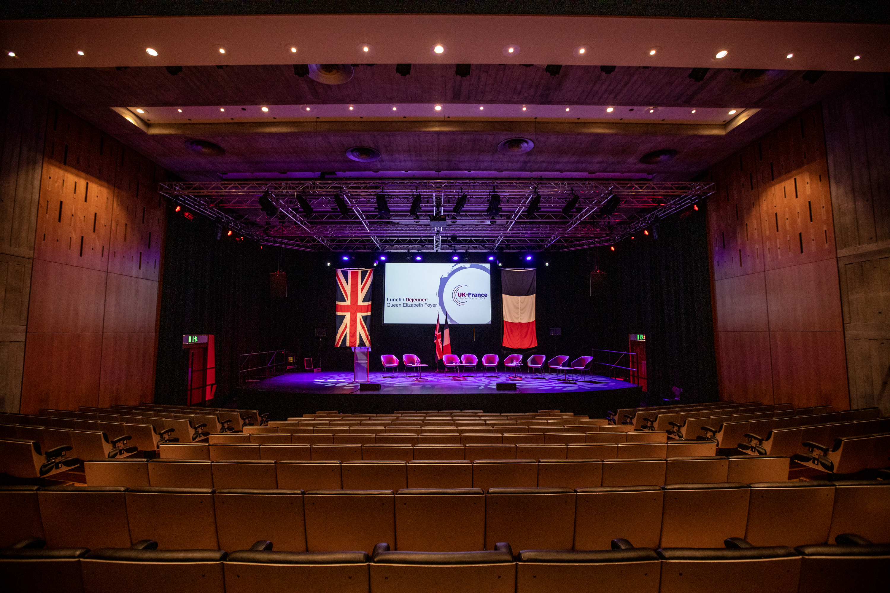 Purcell Room conference setup with stage, seating, and presentation screens. - Banner