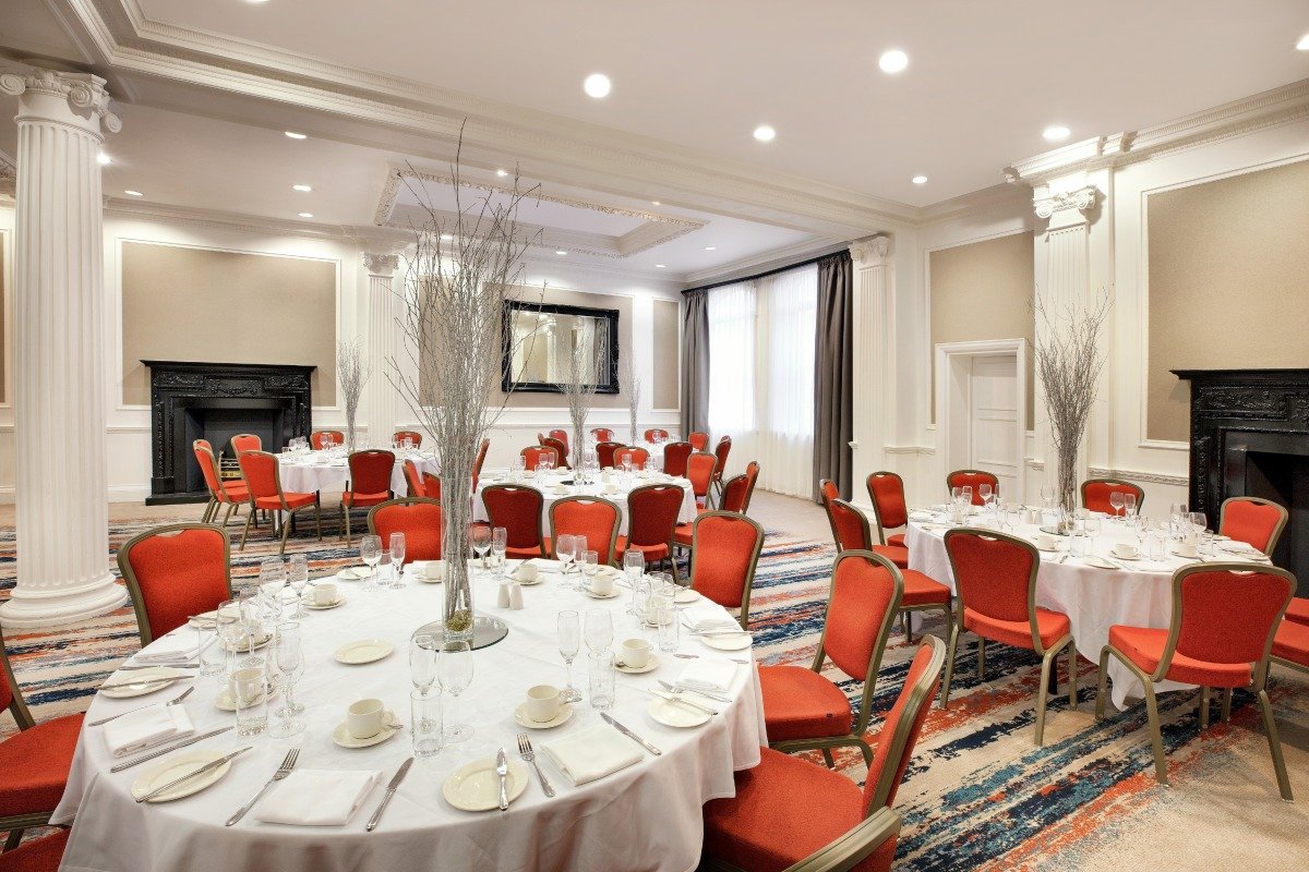 Wedgewood Suite at Leonardo Hotel Cardiff, elegant event space with round tables and red chairs. - Banner