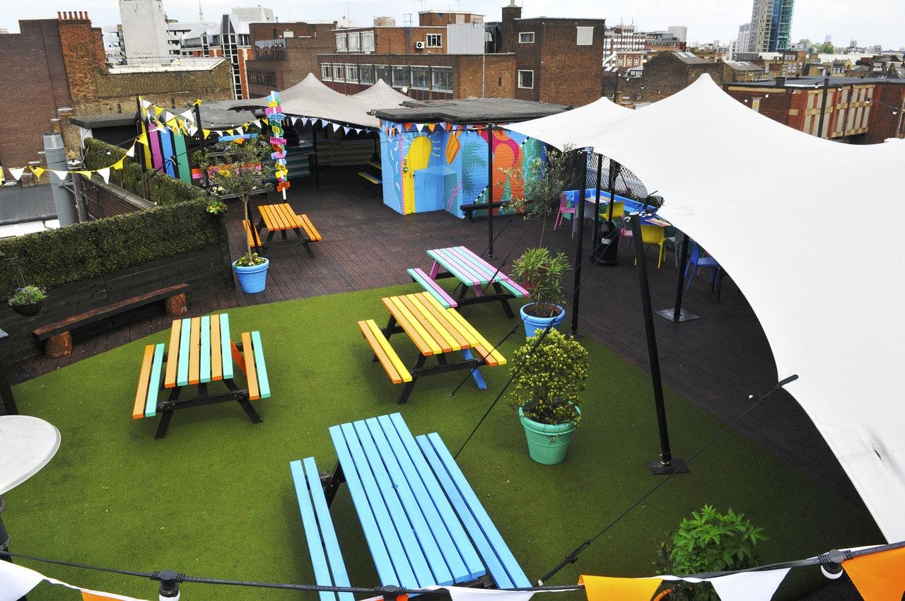 Vibrant rooftop bar space with colorful picnic tables for summer parties and gatherings.