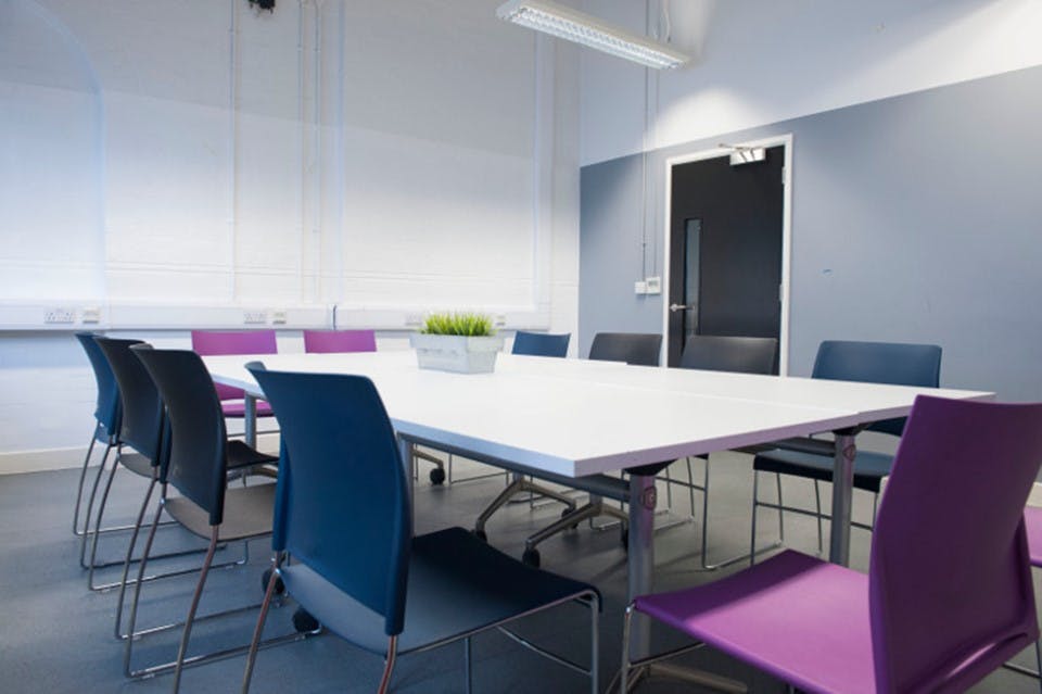 Modern meeting room with large white table and colorful chairs, perfect for collaboration.