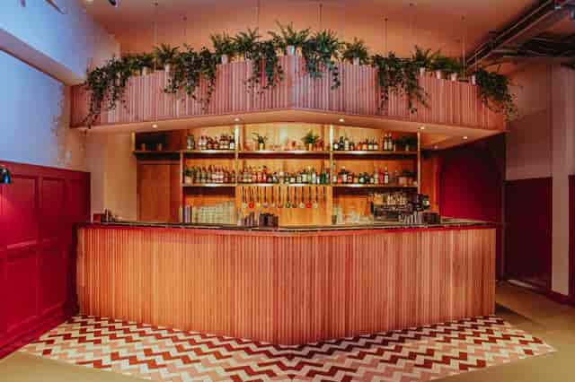 Stylish bar with warm wood tones and greenery, ideal for networking events and cocktail receptions.