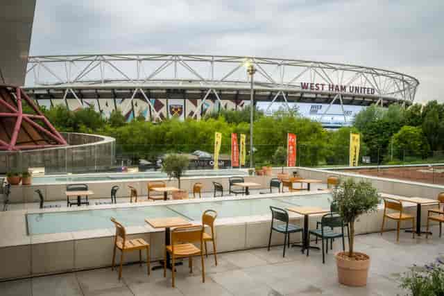 Outdoor networking space at The Yard, with West Ham stadium backdrop and inviting greenery.