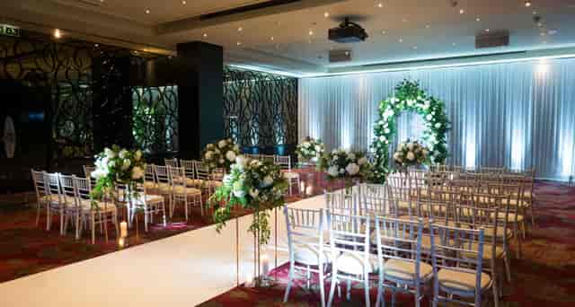 Wedding ceremony setup in The May Fair Crystal Room with silver chairs and floral decor.