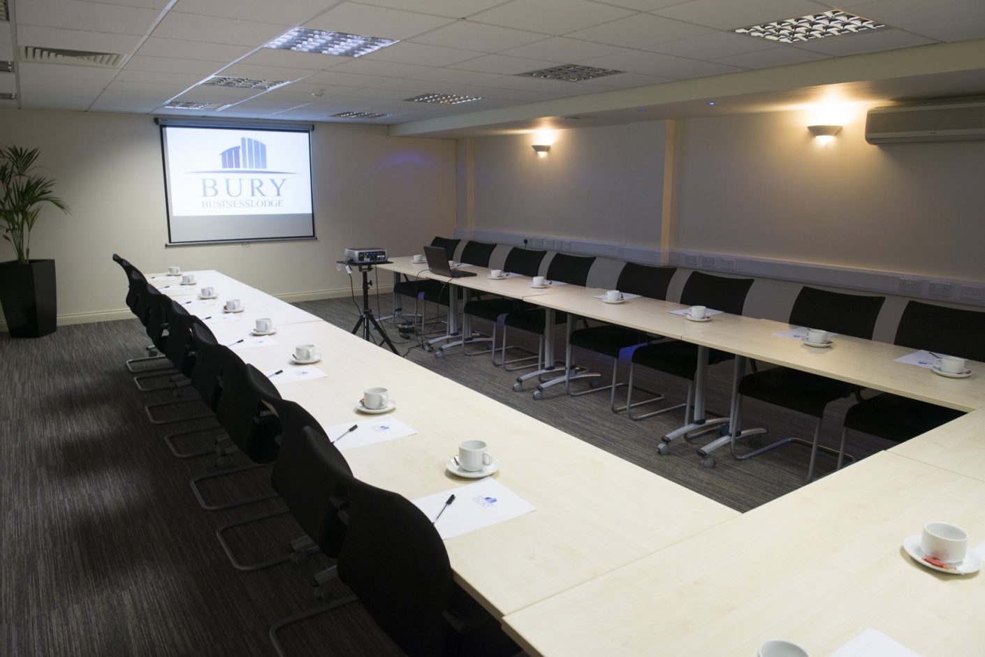 Meeting room with long table setup, projector screen for professional events. - Banner