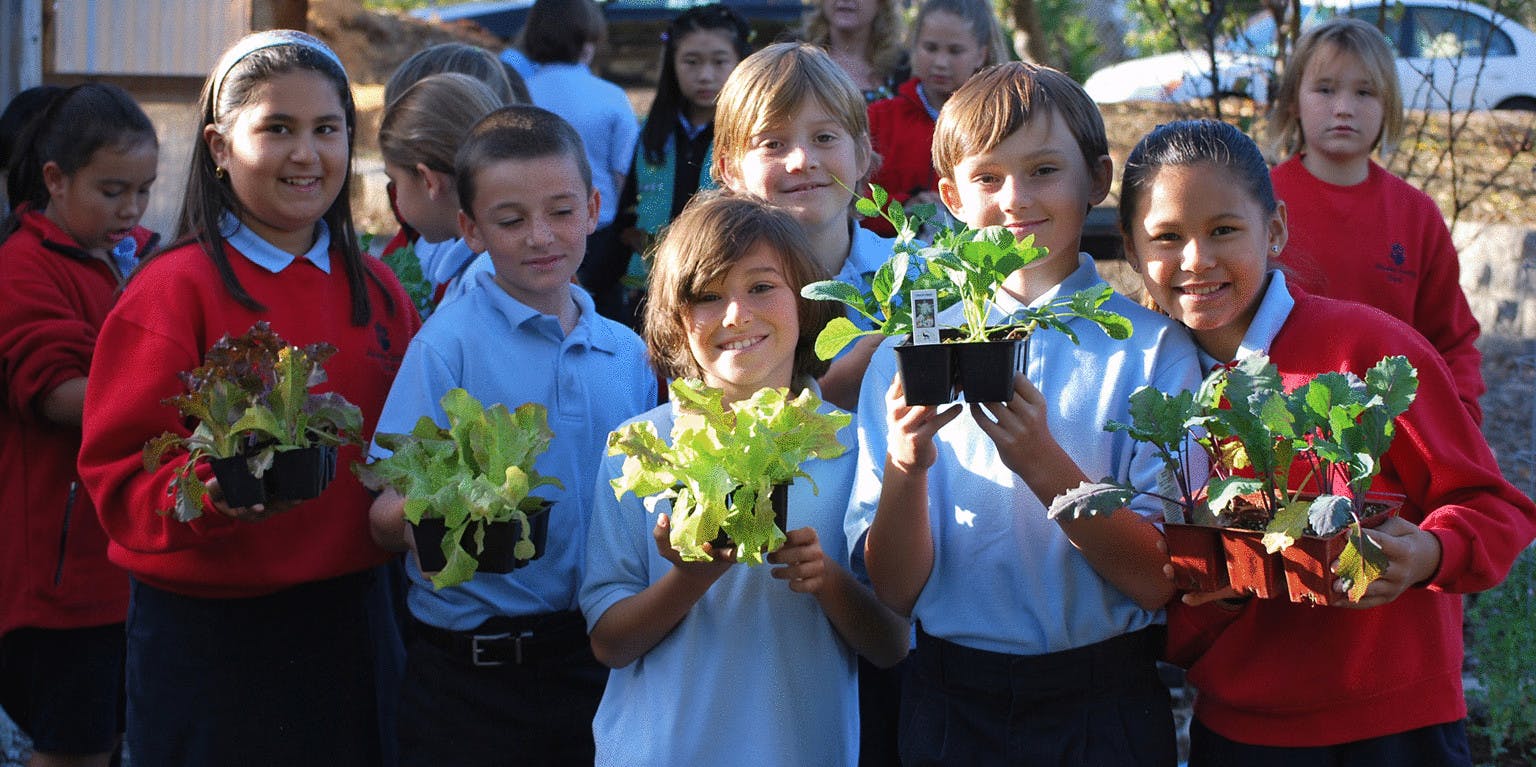 Children with potted plants in Fisher Event Center, promoting teamwork and sustainability.