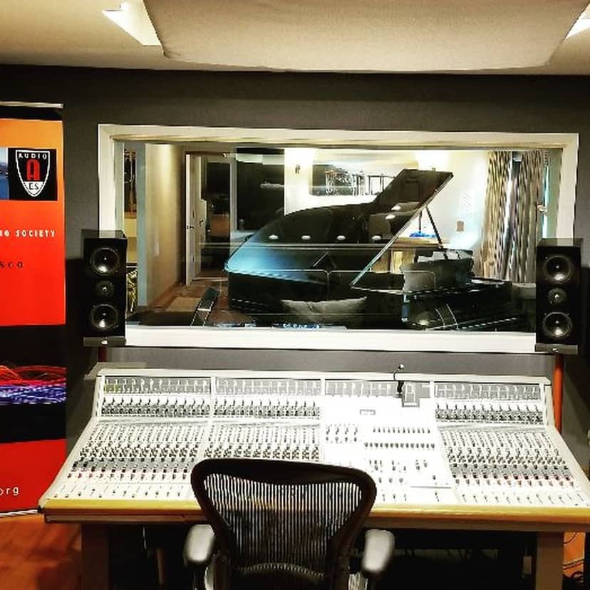 Professional recording studio with mixing console and grand piano for music events.