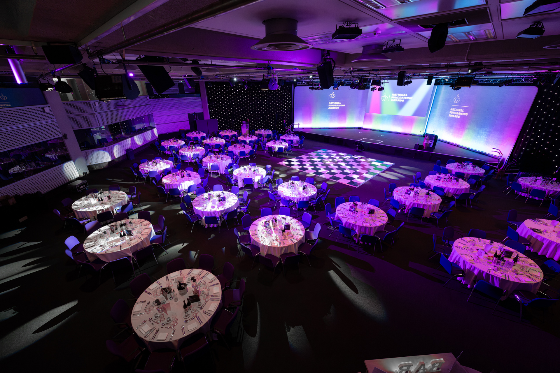 Formal event space at QEII Centre with round tables and stylish stage, ideal for gatherings. - Banner