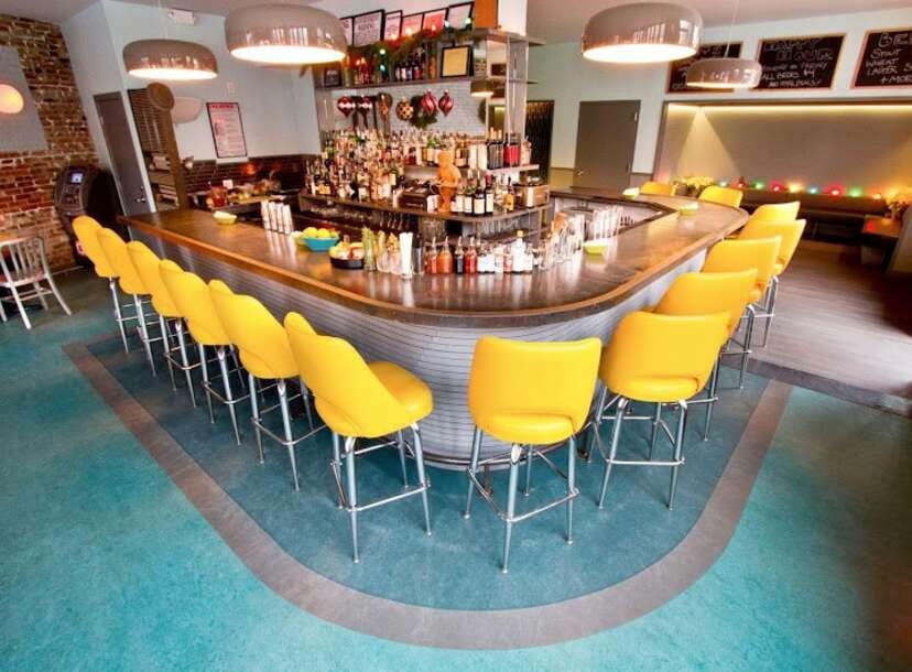 Vibrant Bearded Lady lounge with sleek bar and bright yellow seating for events.