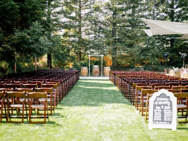Outdoor wedding ceremony at Fortino Winery with rustic wooden chairs and elegant archway.