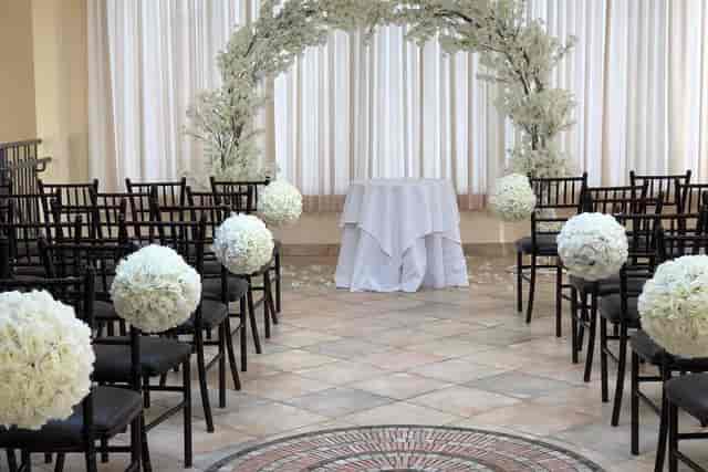 Elegant wedding ceremony setup with white flowers and black chairs at Quixotic Fiestas.